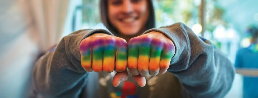 Persona LGBTQ+ mostrando las manos pintadas de arco iris para el Festival del Orgullo de OC